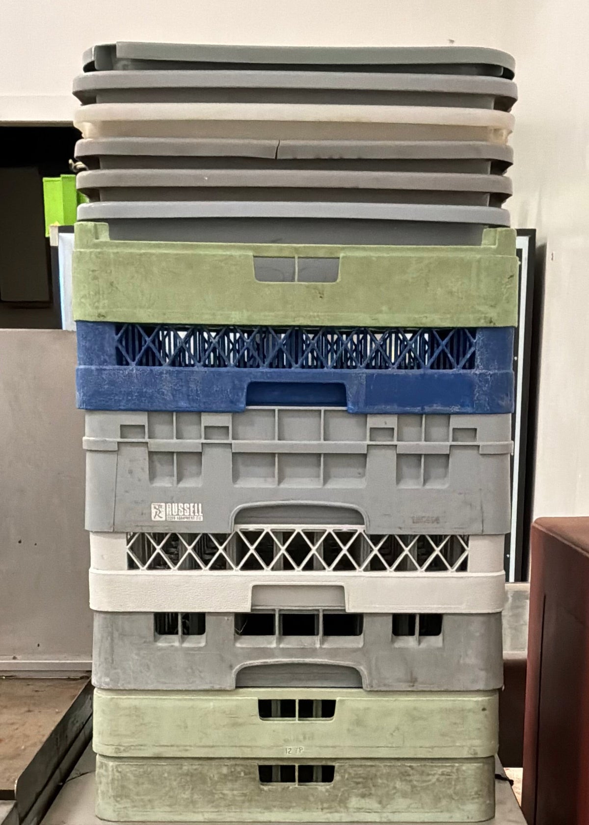 A Jet-Techn commercial dishwasher with a tall stack of assorted plastic storage bins on top, photographed in a utilitarian indoor setting.